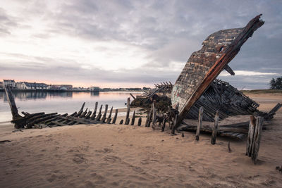 Wooden posts on beach against sky during sunset