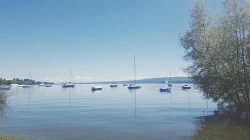 Boats in calm lake against clear sky