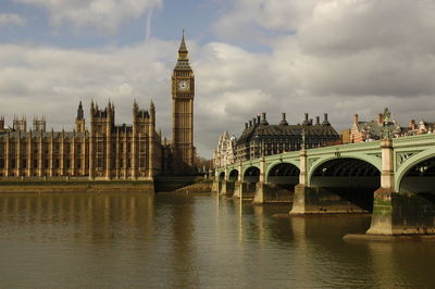 Westminster bridge over thames river by big ben against cloudy sky