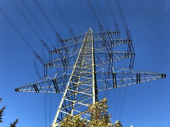 Low angle view of electricity pylon against blue sky