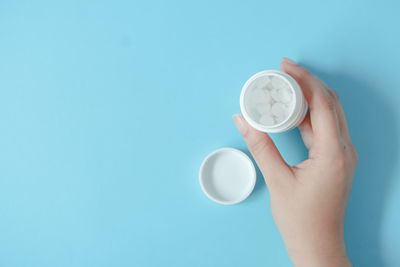 Cropped hand holding clock against blue background