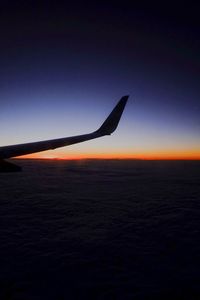 Airplane wing against sky at sunset