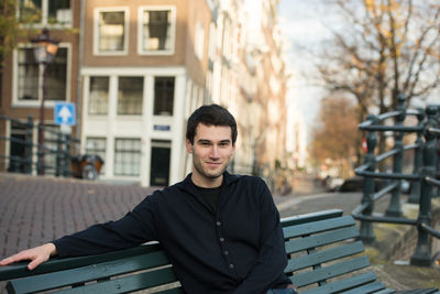 Portrait of smiling young man sitting on bench in city