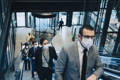 Male and female professionals moving upwards on escalator during covid-19