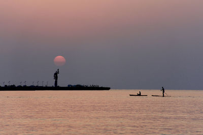 Silhouette birds flying over sea against sky during sunset