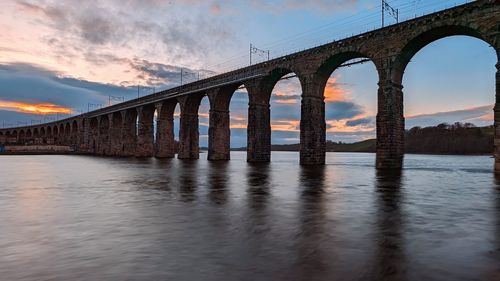 Bridge over river against sky during sunset