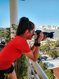 Side view of woman photographing against sky