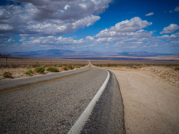 Empty road by mountains against cloudy sky