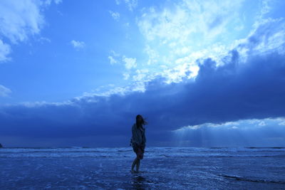 Woman standing at beach against blue sky