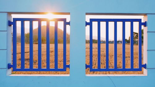 Mountain and sky seen through metal fence on blue wall 