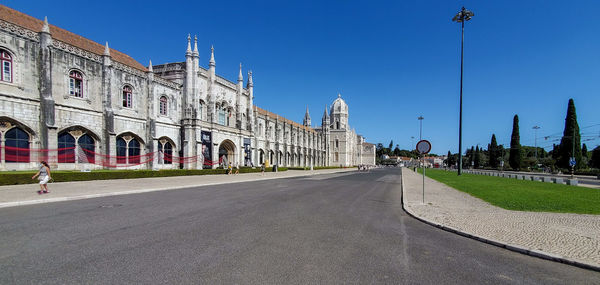 Road passing through city against clear blue sky