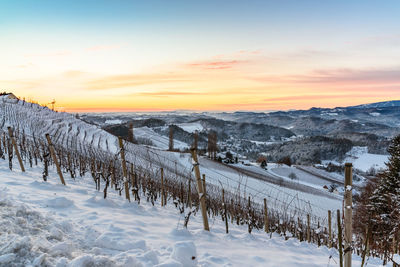 Snow covered field against sky during sunset