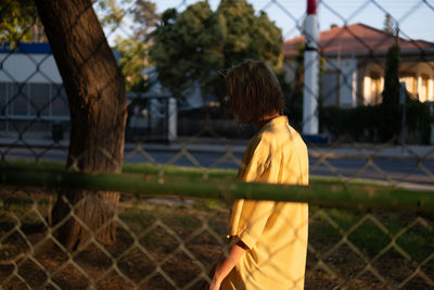 Rear view of man standing by chainlink fence