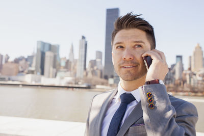 Portrait of a young businessman talking on his smartphone on a rooftop overlooking the city