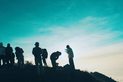 Silhouette people standing on rock against sky during sunset