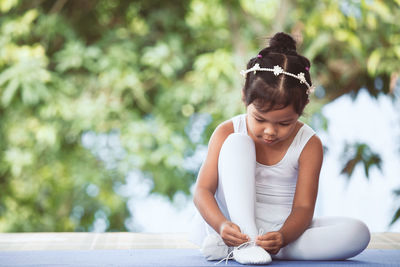 Full length of girl tying ballet shoelace against plants