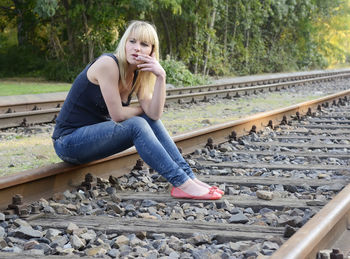 Full length of woman smoking while sitting on railroad track