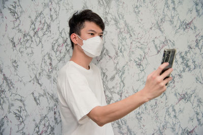 Man holding mobile phone while standing against wall