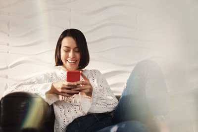 Smiling young woman using smart phone while sitting on laptop