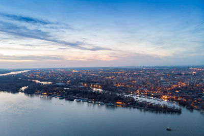 High angle view of illuminated buildings by river against sky