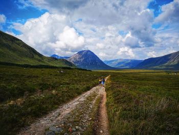 Man cycling on road amidst field against sky