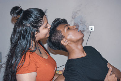 Side view of smiling woman looking at man emitting smoke