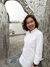 Portrait of smiling young woman standing against water