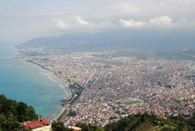 Aerial view of cityscape and sea against cloudy sky