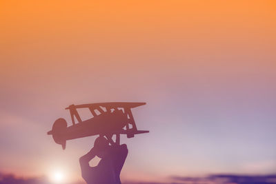 Silhouette person holding umbrella against sky during sunset