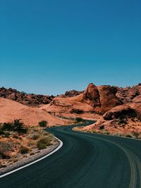 Road amidst red desert against clear blue sky
