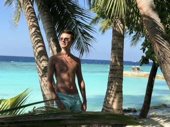 Young man standing on palm tree trunk by sea