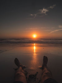 Low section of people on beach against sky during sunset