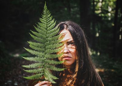Portrait of young woman holding leaves in forest