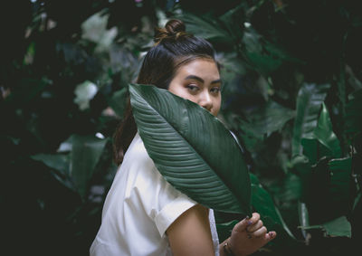 Portrait of young woman covering mouth with leaf against plants