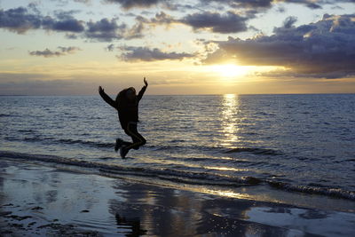 Woman jumping on beach against sky during sunset