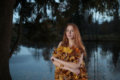 Young woman with autumn leaves against lake