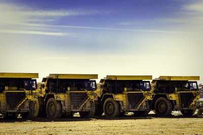 Four yellow dumper trucks in mine put in row, with blue sky background and clouds