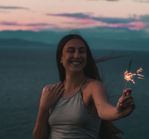 Portrait of young woman smiling against sky during sunset