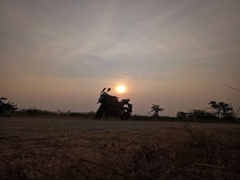 Man riding bicycle on field against sky during sunset