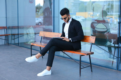 Young businessman using digital tablet sitting on bench outdoors