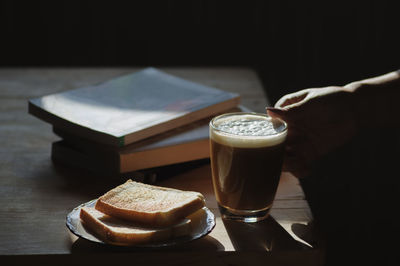 Close-up of hand holding coffee cup by toasted bread and books on table