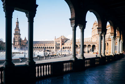 Historic buildings at plaza de espana seen through colonnade against blue sky