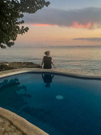 Swimming pool by sea against sky during sunset