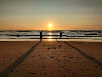 Silhouette people on beach against sky during sunset