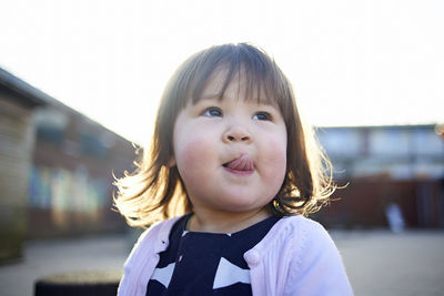 Girl looking away while sticking out tongue on footpath