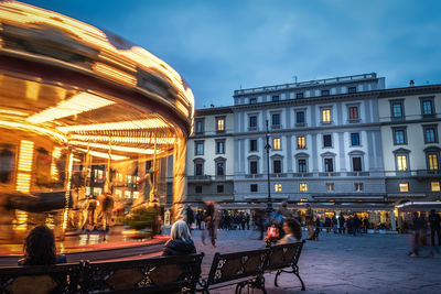 People walking on illuminated street in city at dusk