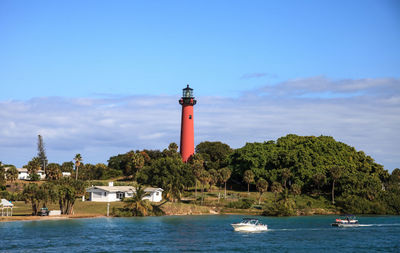 Lighthouse amidst sea and buildings against sky