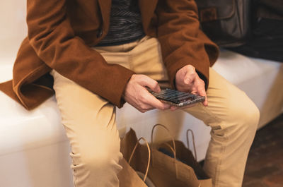 A young man with a phone in his hands is sitting on a bench in a store.