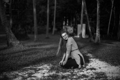 Portrait of beautiful woman kneeling against trees