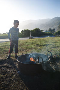 Full length of boy roasting marshmallows in campfire on field